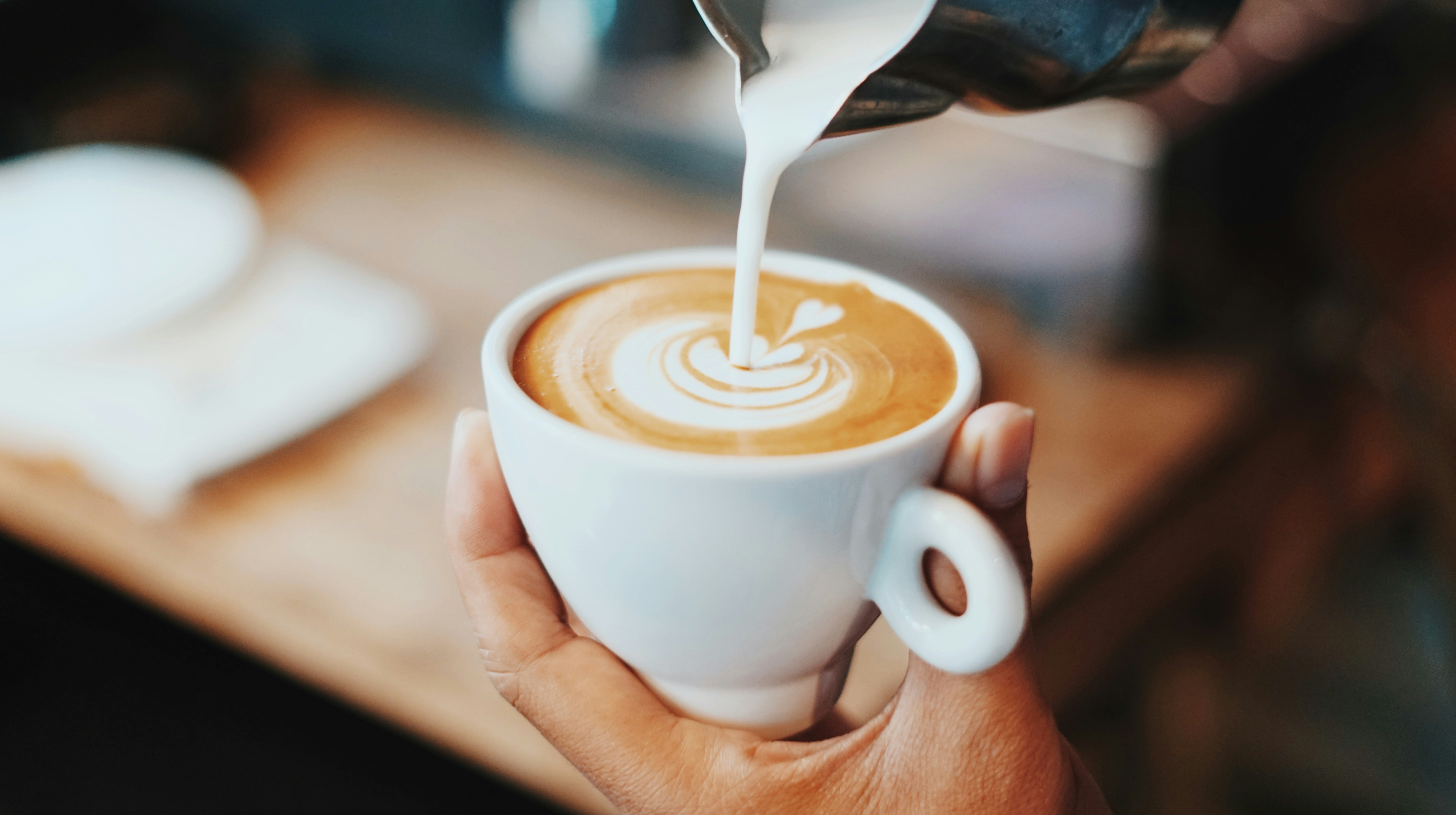 Milk being poured into a cup of latte held in a hand